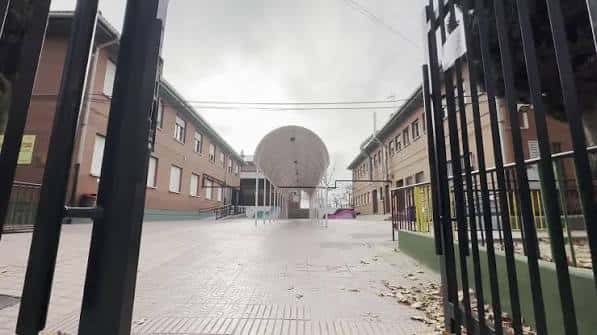 Entrada al recinto escolar desde la calle, con portón metálico abierto y vista del patio interior
