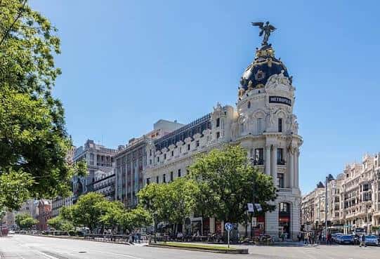 Perspectiva amplia del Edificio Metrópolis desde la calle, rodeado de árboles y tráfico urbano