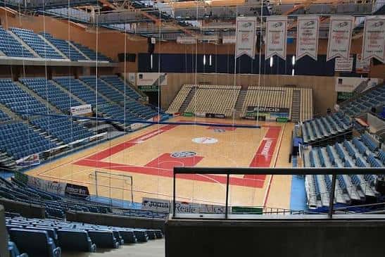 Interior del pabellón deportivo con pista de baloncesto y gradas azules