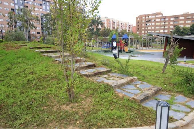 Área verde del parque con senderos de piedra y zona de juegos al fondo