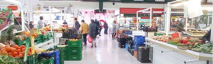 Interior del mercado con puestos de frutas y verduras y clientes caminando