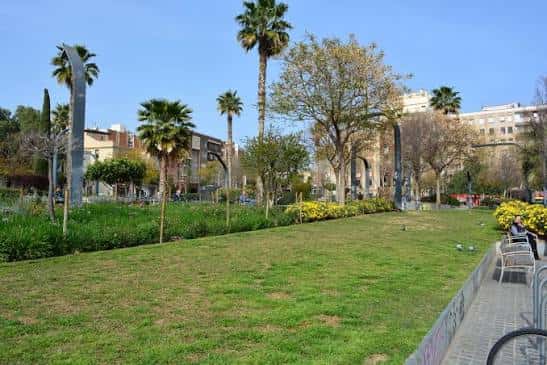 Vista general de la Plaça de Pompeu Fabra con zonas verdes y palmeras