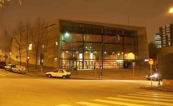 Fachada principal de la biblioteca iluminada por la noche, destacando el uso de vidrio y luz interior