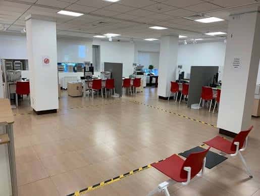 Interior amplio y ordenado de la oficina con mostradores, sillas rojas y señalización de distanciamiento