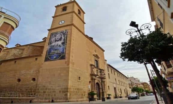 Fachada principal de la Iglesia de San Francisco con cartel religioso y reloj en la torre