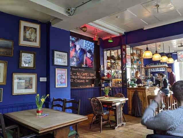Interior acogedor del pub con paredes azules, mesas de madera y barra iluminada