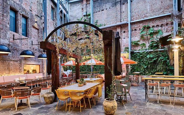 Patio exterior del The Lucky Hotel con mesas y sillas bajo un arco de madera