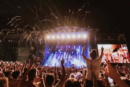 Público en primer plano con las manos levantadas frente al escenario iluminado durante el concierto