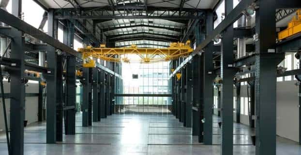 Interior del recinto ferial con vigas industriales y grúa amarilla en el techo