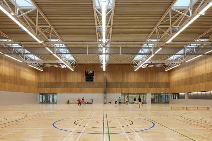 Gimnasio principal con suelo de madera y estructura metálica en el techo