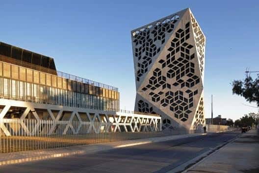 Fachada moderna del edificio con patrón hexagonal y puente peatonal adyacente al atardecer