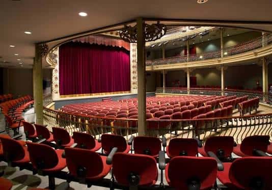 Interior del teatro con butacas rojas y cortina de escenario