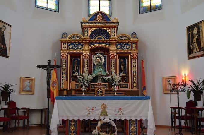 Interior de la ermita mostrando el altar principal con la imagen de la Virgen y decoración floral