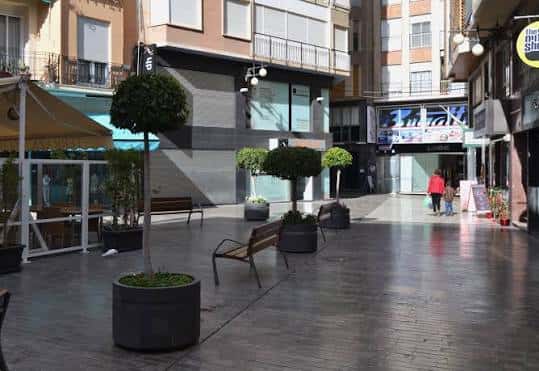 Vista de la plaza peatonal con bancos y árboles en macetas