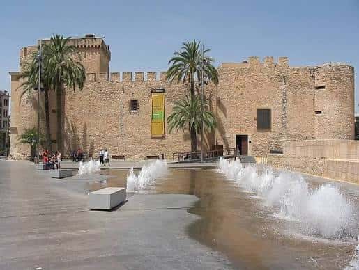 Castillo de Elche con fuentes y palmeras en primer plano