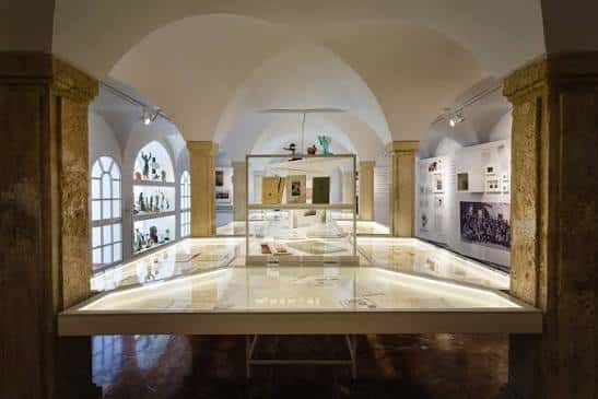 Sala de exposiciones con vitrinas iluminadas y bóvedas de piedra