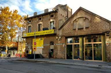 Vista lateral del edificio de BiciHub Can Picó con entrada principal y cartel amarillo