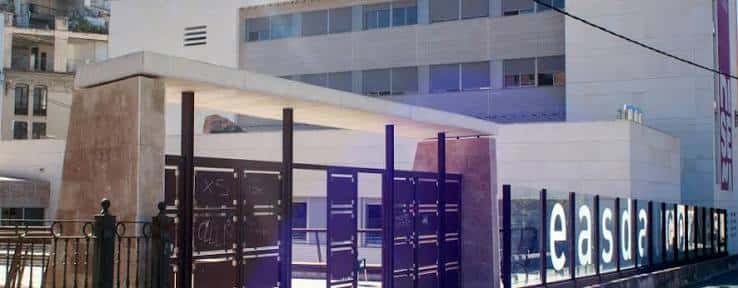 Entrada principal de la escuela con portones metálicos y señalización 'easda' en la pared