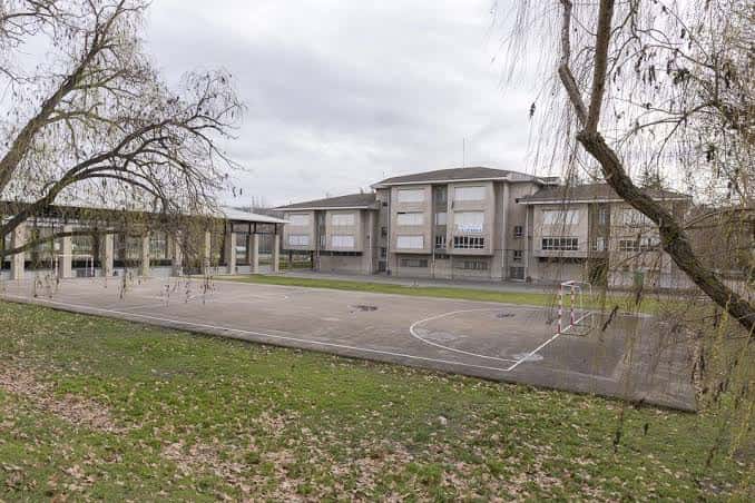 Vista general del edificio escolar desde el exterior con árboles y cancha deportiva