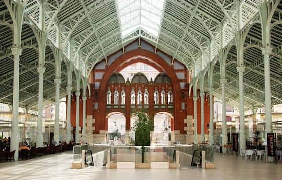 Interior del mercado mostrando la estructura metálica blanca, techos altos y arcos centrales bajo luz natural