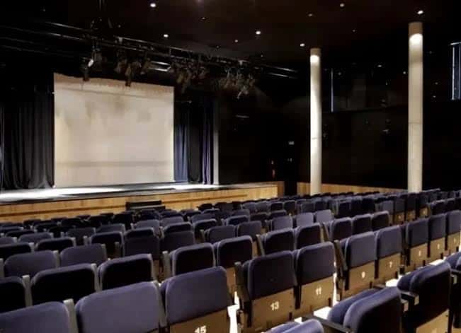 Interior del auditorio principal con butacas azules y escenario equipado para eventos