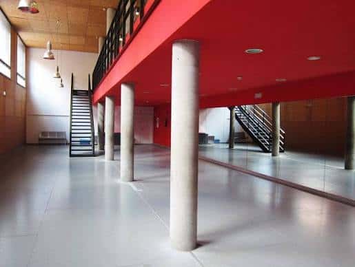 Espacio interior versátil con suelo reflectante y estructura roja ideal para actividades culturales