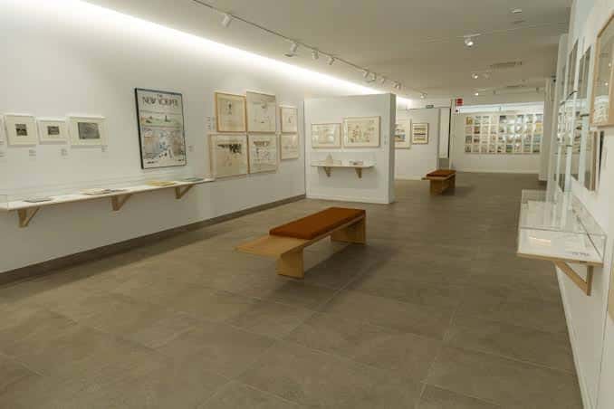 Espacio expositivo amplio con vitrinas, bancos y murales de Saul Steinberg