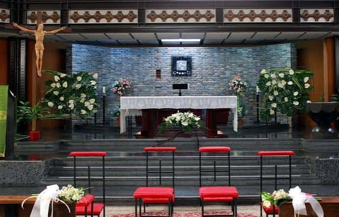 Interior del altar principal decorado con flores blancas y crucifijo para ceremonias