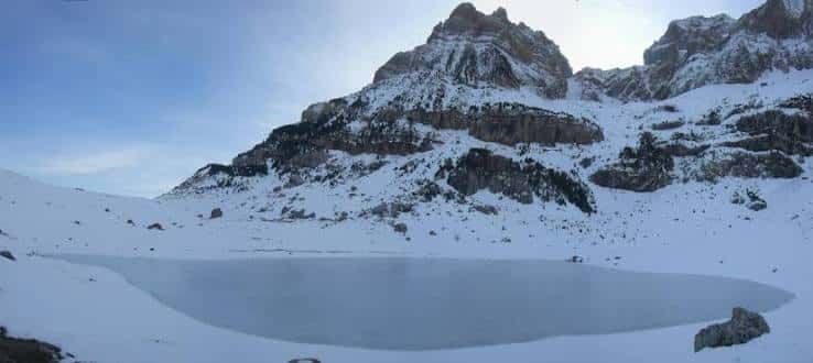 Ibón de Piedrafita congelado en invierno rodeado de nieve y picos montañosos