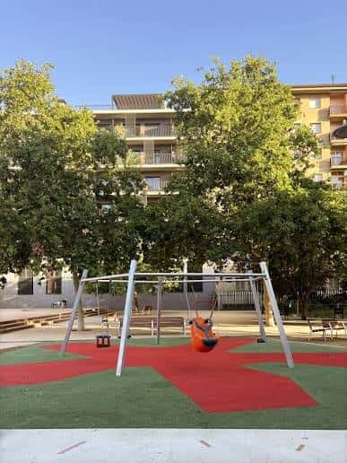 Columpios modernos en un parque infantil rodeado de árboles y edificios residenciales