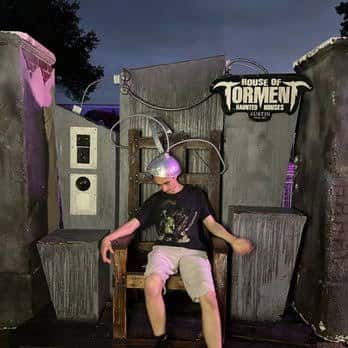 Persona sentada en una silla de tortura frente a la entrada del House of Torment