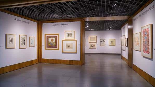 Interior de la sala de exposiciones con obras enmarcadas y paredes blancas