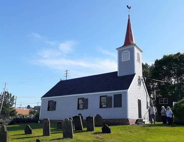 Vista exterior de la Little Dutch Church en un día soleado con césped verde y lápidas antiguas al frente