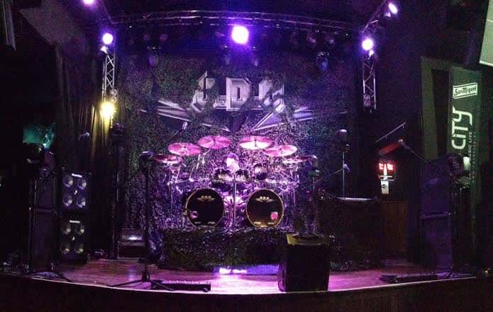 Escenario vacío de la sala con iluminación púrpura y batería montada