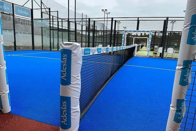 Campo de pádel interior con red y postes protegidos por fundas blancas con logotipo Adeslas
