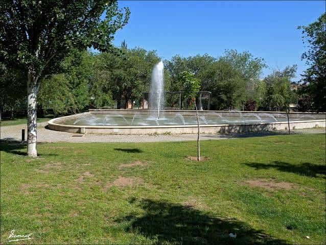 Fuente central del parque rodeada de césped y árboles en un día soleado