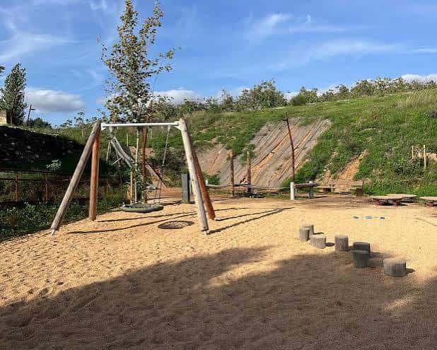 Zona de juegos infantiles con columpios de madera sobre arena