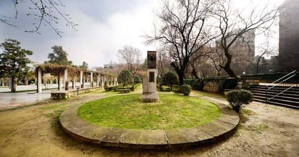 Vista del parque con césped central y monumento en primer plano