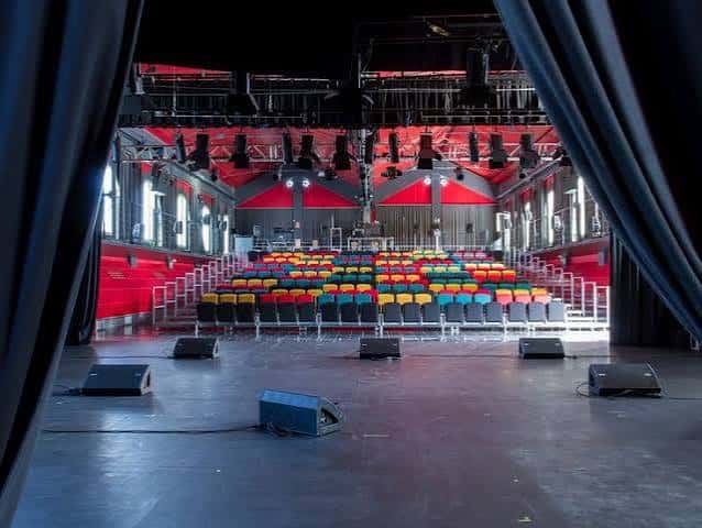 Interior del auditorio con butacas multicolores y escenario preparado para eventos
