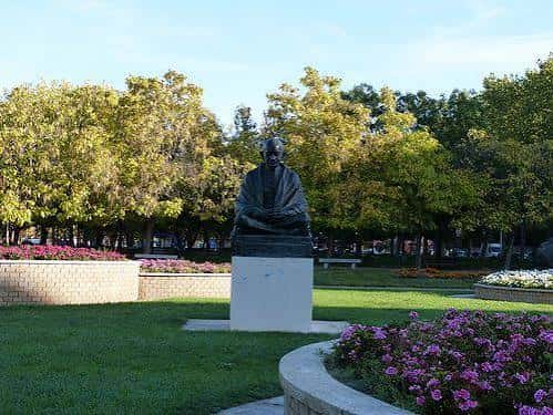 Estatua de Gandhi rodeada de césped y macizos de flores púrpuras