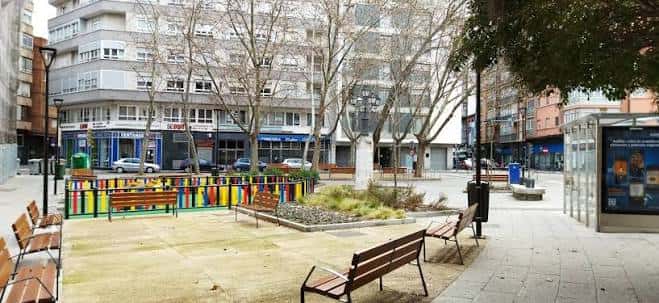 Plaza comunitaria frente al centro con bancos, árboles y zona de juegos infantiles