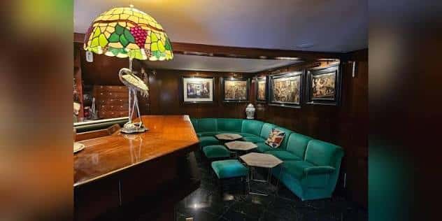 Sala acogedora con sofá verde, lámpara Tiffany y mesas bajas junto a la barra