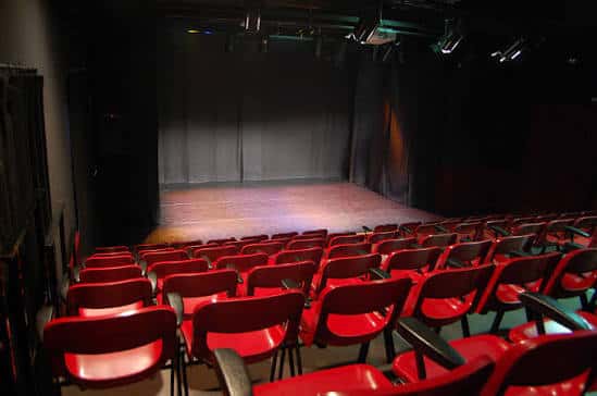 Interior del auditorio con butacas rojas y escenario iluminado