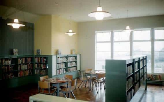 Interior de la biblioteca con estanterías verdes y mesas de lectura