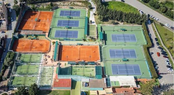 Perspectiva cenital del complejo deportivo con múltiples pistas de tenis y pádel en diferentes colores