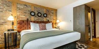 Habitación doble con cama king-size, cabecero de cuero y pared de ladrillo decorativa