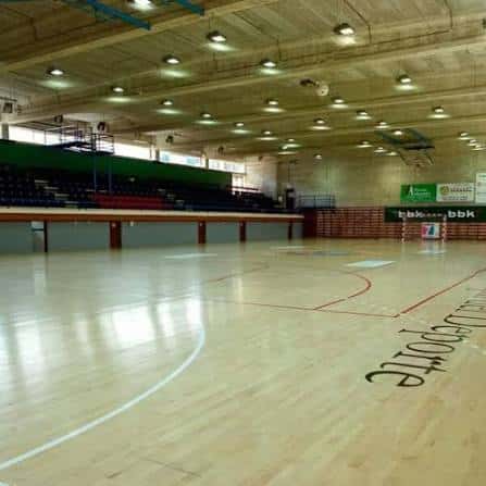 Vista interior del pabellón deportivo con pista de madera y gradas