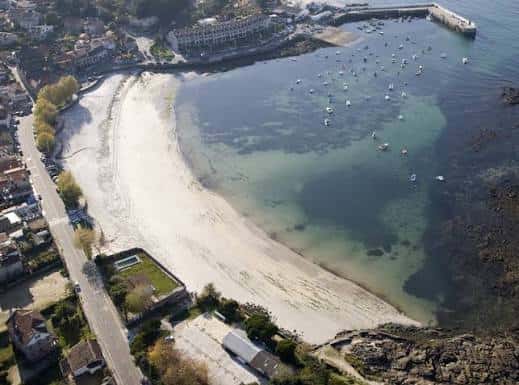 Panorámica elevada de la cala de Canido con embarcaciones ancladas y arena blanca