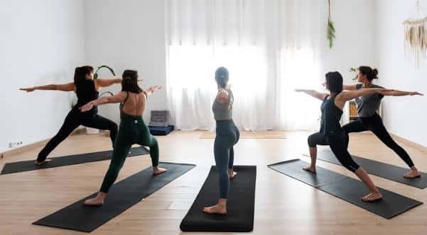 Clase de yoga en grupo con participantes en postura de guerrero en un estudio luminoso
