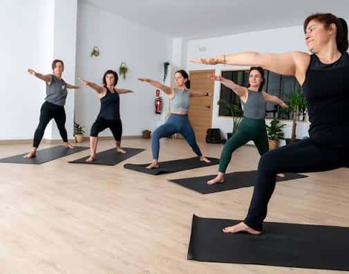 Sesión de yoga grupal con instructora guiando a los alumnos en una sala espaciosa